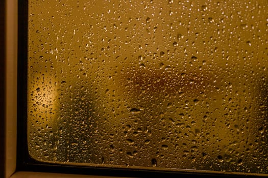 Close up of rain drops on the window in rainy night, warm lights and window frame
