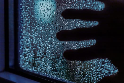 Close up of hand silhouette on window with water drops, night