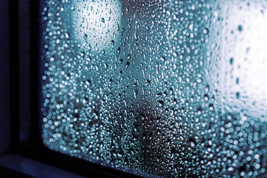 Close up of rain drops on the window in rainy night, cool lights and window frame