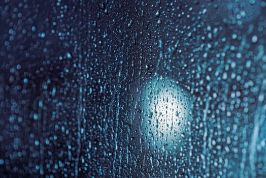 Close up of rain drops on the window in rainy night, cool lights