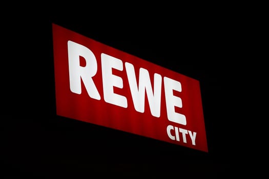 Rewe supermarket chain neon sign in the center of Berlin at night with black background