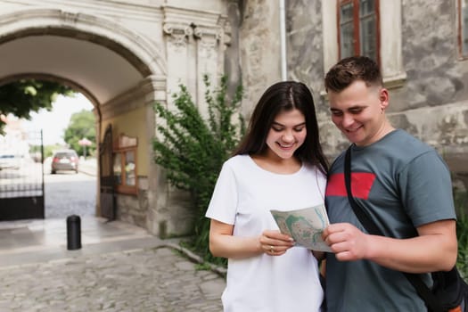 A couple of handsome heterosexual tourists in love looking at a city map to understand how to find a place. The girl points her finger and smiles. Wife and husband have a vacation trip to other city.