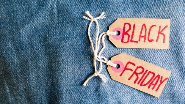 Stylish jeans with a black friday flag. Black friday and cyber monday sale discount concept tag with blue jeans. Black friday written on grunge jeans texture. Background, holiday concept. Black Friday - International day of shopping, promotions, discounts, sales. The sales season is the fourth Thursday of November. Copy space, place for text, flat lay.