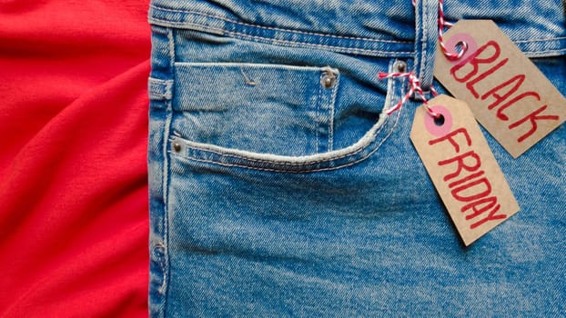 Stylish jeans with a black friday flag. Black friday and cyber monday sale discount concept tag with blue jeans. Black friday written on grunge jeans texture. Background, holiday concept. Black Friday - International day of shopping, promotions, discounts, sales. The sales season is the fourth Thursday of November. Copy space, place for text, flat lay.