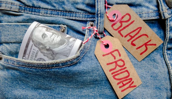 Money dollars in a lot in jeans pocket and cardboard tag with text black friday. Blue background, holiday concept. Black Friday - International day of purchases, promotions, discounts, sales. The sales season is the fourth Thursday of November. Copy space, place for text, flat lay.