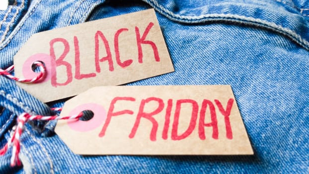 Stylish jeans with a black friday flag. Black friday and cyber monday sale discount concept tag with blue jeans. Black friday written on grunge jeans texture. Background, holiday concept. Black Friday - International day of shopping, promotions, discounts, sales. The sales season is the fourth Thursday of November. Copy space, place for text, flat lay.