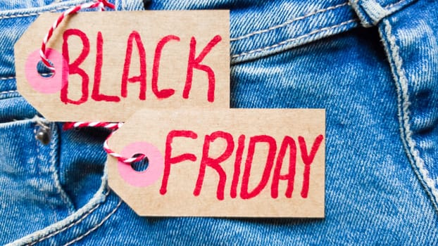 Stylish jeans with a black friday flag. Black friday and cyber monday sale discount concept tag with blue jeans. Black friday written on grunge jeans texture. Background, holiday concept. Black Friday - International day of shopping, promotions, discounts, sales. The sales season is the fourth Thursday of November. Copy space, place for text, flat lay.