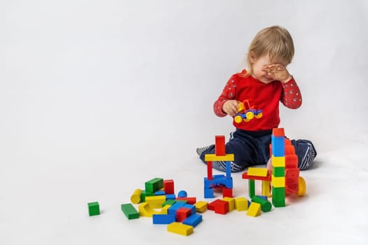 Crying little boy is playing with colorful wooden cubes sitting on the floor.