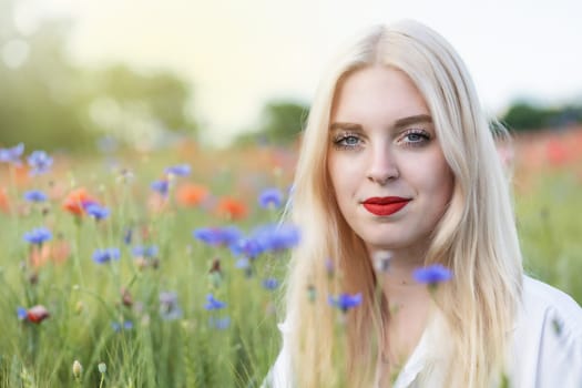 Portrait of attractive blonde woman in cornflower and poppy meadow. Horizontally.