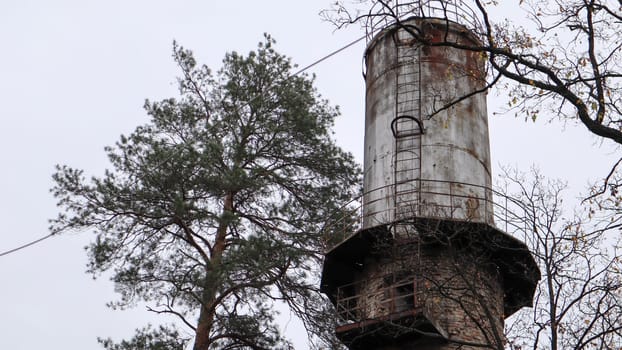 The pipe of the plant rise above the forest. Industrial landscape. Ecological production without smoke from pipes. Water tower in the village. Water supply to houses under a pressure. Rural landscape