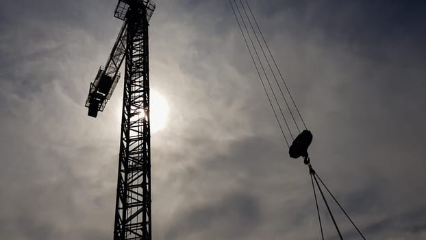 Construction crane on a background of blue sky. Close view of a construction crane. Abstract industrial background with a silhouette of a construction crane over the sky with clouds