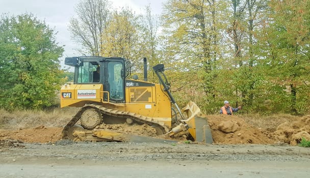 Ukraine, Kiev - October 1, 2019: Road roller, tractor and construction equipment are working on a new road construction site. The road is closed for road repair, route extension, pothole repair.