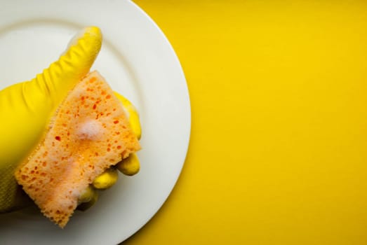Cleaning sponge on a white plate on a yellow background.