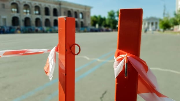 Red white does not cross the tape and the metal pole. Signal red and white tape hanging on a metal fence, danger, warning. Ribbon and metal red post. Forbidden tape encloses an unsafe area