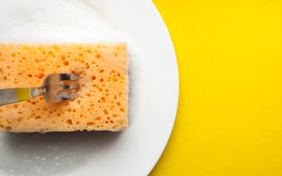 Cleaning sponge on a white plate on a yellow background.