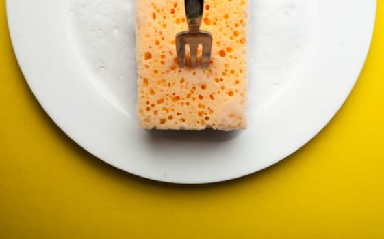 Cleaning sponge on a white plate on a yellow background.