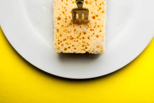Cleaning sponge on a white plate on a yellow background.