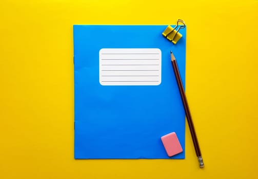 Blue mock up notebook and textbook butt for school subjects, eraser, pencil, paper clip on a yellow background. Flat lay, copy space, top view, place for text