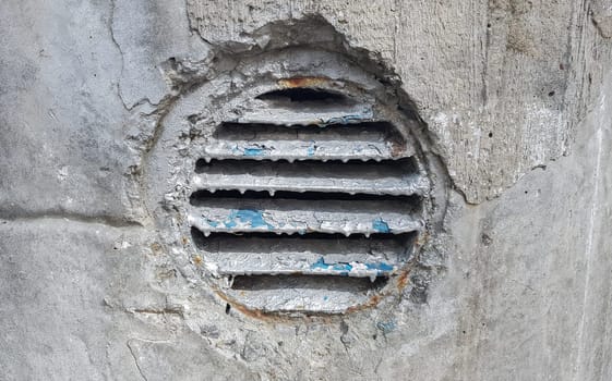 ventilation hole in concrete. Metal industrial round ventilation cover. Rusty and dirty old round ventilation frame with horizontal metal stripes
