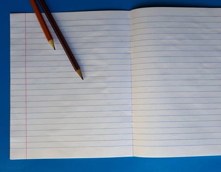 Open notebook on a white lining on a blue wooden tabletop with a pencil.