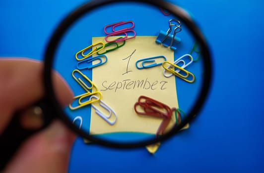 September 1st Day Concept. September 1, calendar with magnifier on a blue background and paper clips.