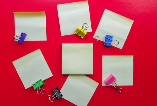 Blank yellow sticky notes and paper clip clips on a red background, business work concept. Yellow commemorative stickers on the red wall. Layout.