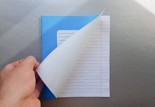 Design concept - Top view of a high quality male hand leafing through a sheet of blue striped notebook. Top view, copy space, flat lay.