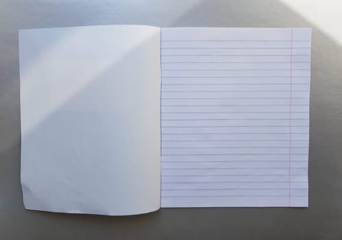 open school notebook with pen on a gray desk with sun rays from the window. A blank, white sheet of notebook for writing. education concept. Copy space. view from above. Flat lay.
