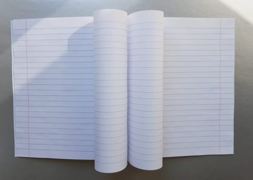 open school notebook with pen on a gray desk with sun rays from the window. A blank, white sheet of notebook for writing. education concept. Copy space. view from above. Flat lay.