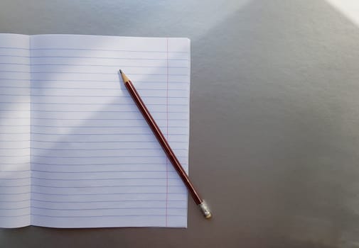 open school notebook with pen on a gray desk with sun rays from the window. A blank, white sheet of notebook for writing. education concept. Copy space. view from above. Flat lay.