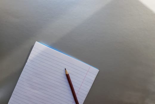 open school notebook with pen on a gray desk with sun rays from the window. A blank, white sheet of notebook for writing. education concept. Copy space. view from above. Flat lay.