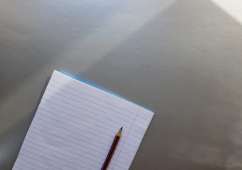 open school notebook with pen on a gray desk with sun rays from the window. A blank, white sheet of notebook for writing. education concept. Copy space. view from above. Flat lay.
