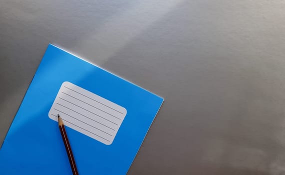 New blue notebook with pencil on a gray table with sun rays from the window background.