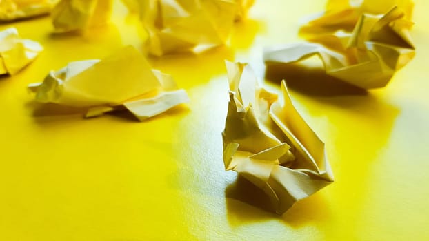 Ball crumpled paper ball isolated on a yellow background. Crumpled paper for texture. Crumpled paper after a brainstorming was thrown into the bin. A piece of yellow crumpled paper on a yellow background