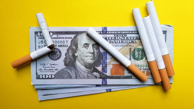 Classic cigarettes stand on one hundred US dollar bills. Cigarettes on a hundred dollar bill on a yellow background.