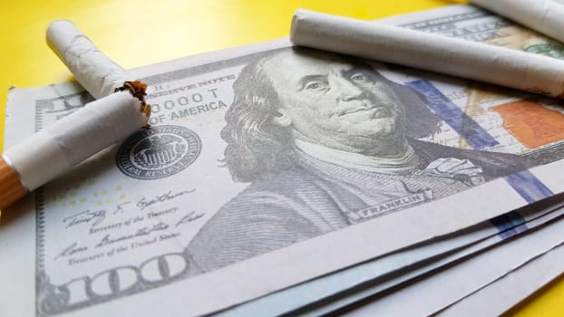 Classic cigarettes stand on one hundred US dollar bills. Cigarettes on a hundred dollar bill on a yellow background.