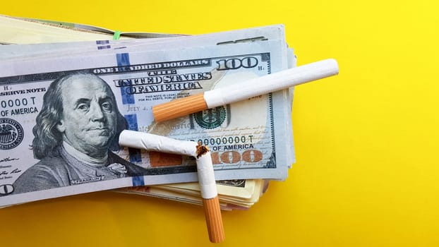 Classic cigarettes stand on one hundred US dollar bills. Cigarettes on a hundred dollar bill on a yellow background.