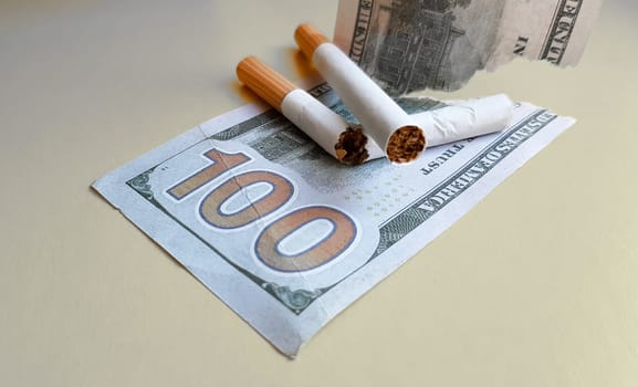 Classic cigarettes stand on one hundred US dollar bills. Cigarettes on a hundred dollar bill on a yellow background.