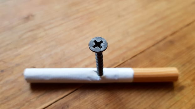 Screw and yellow background. Screw screwed into a cigarette. Anti-smoking concept.