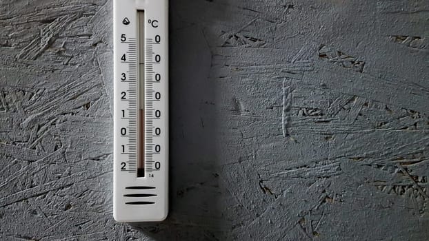 white thermometer hanging on a gray gray wooden wall indoors, background with copy space and empty place for your text.
