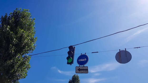 Traffic light and signs on the street close up with a burning green light.