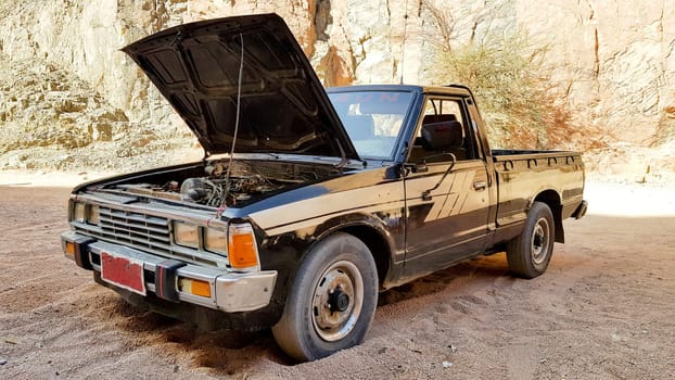 Egypt, Sharm El Sheikh - June 7, 2019: an old black pickup truck in the desert with an open hood.