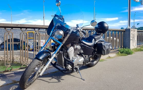 Ukraine, Kiev - September 08, 2019: Black vintage motorcycle parked on a bridge in the city center surrounded by city center buildings of urban environments. Hipster style, student dream, wild lifestyle.