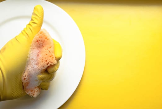 Cleaning sponge on a white plate on a yellow background.