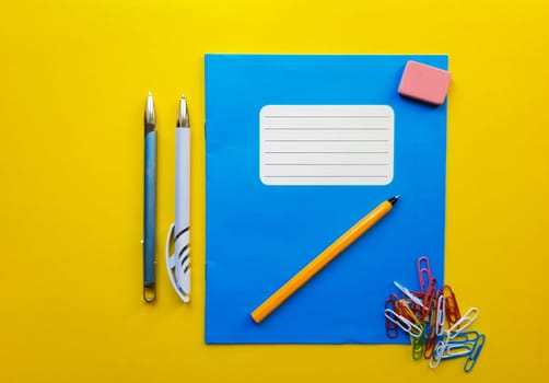 Blue mock up notebook and textbook butt for school subjects, eraser, pencil, paper clip on a yellow background. Flat lay, copy space, top view, place for text