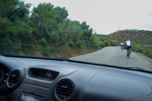 Driving slowly behind cyclists at country curvy road. View from the inside of the car