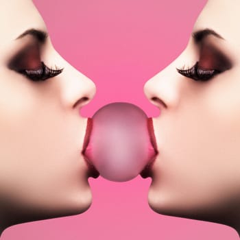 Sexy young woman makes a balloon with a bubble gum against pink background