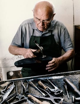 Old shoemaker adjusts the sole of a shoe