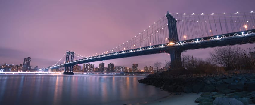 Manhattan bridge and New York City downtown skyline at dusk with skyscrapers illuminated over East River panorama. Copy space.