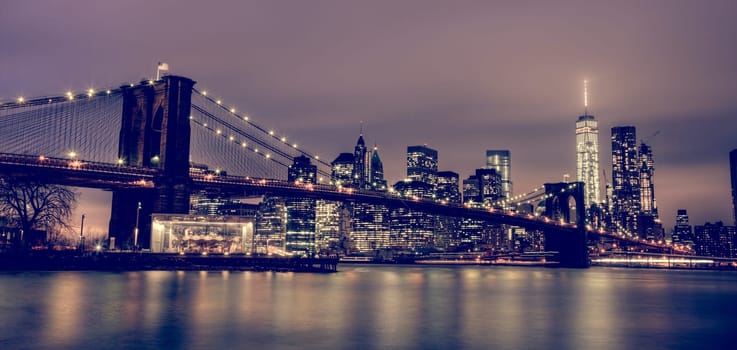 Brooklyn bridge and New York City Manhattan downtown skyline at dusk with skyscrapers illuminated over East River panorama. Copy space.